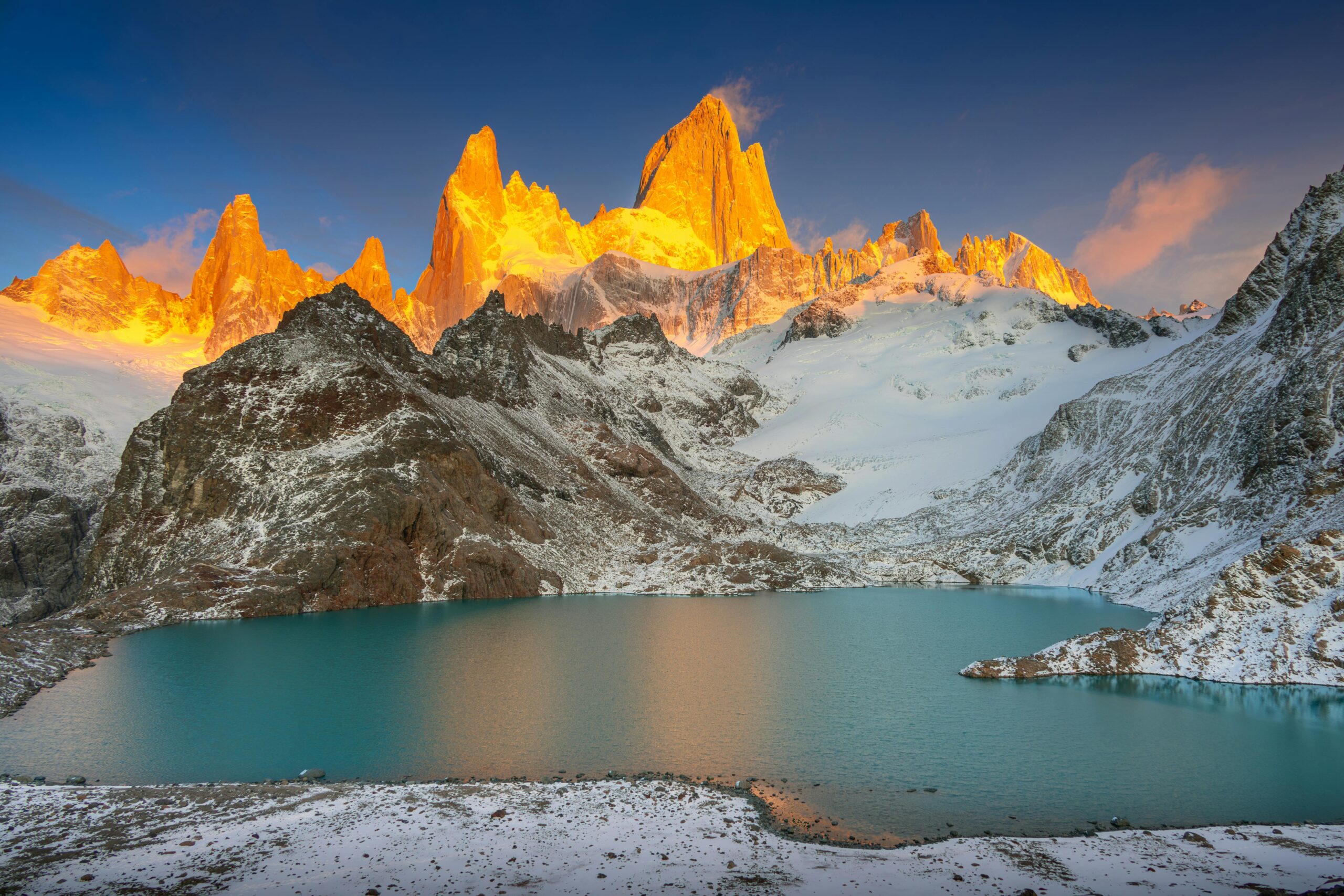 A stunning winter landscape featuring glowing mountains and a serene lake at sunrise.