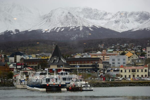 A scenic view of Ushuaia port in Argentina with boats and snow-capped mountains in the background.